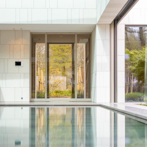 Luxe beige stalen buitendeuren met glas, grenzend aan een moderne villa met zwembad.